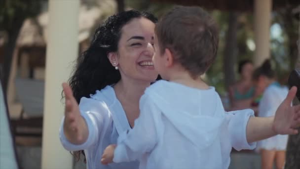 Gelukkige moeder knuffelen haar kind aan de kust. Schattig kind kusjes zijn moeder en zachtjes knuffels. Concept moeder met een kind buitenshuis, gelukkige familie, gelukkige kindertijd, kleine baby. — Stockvideo