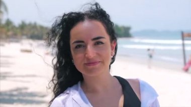 Güneş gözlüğü genç kadın veya neşeli kız kamera bakıyor ile Avrupa güzel sevimli esmer bir tropikal Plaj yakın çekim portre, Rüzgar saç rüzgar, yavaş hareket üfleme.