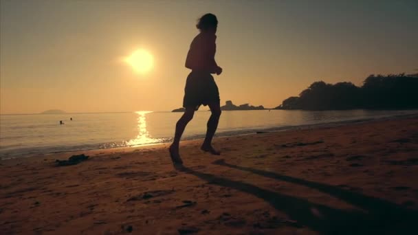Mladý muž atlet běží na délku pláže na pozadí západu slunce, intenzivní kardiochirurgický trénink, tropické pozadí, pomalý pohyb. Koncepce zdraví, sportu, cvičení kardio. — Stock video
