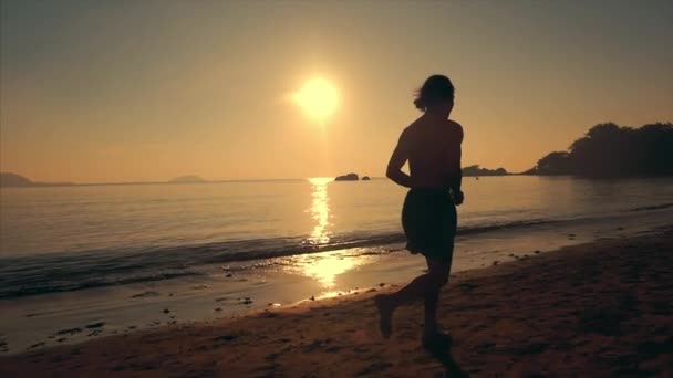 Mladý muž atlet běží na délku pláže na pozadí západu slunce, intenzivní kardiochirurgický trénink, tropické pozadí, pomalý pohyb. Koncepce zdraví, sportu, cvičení kardio. — Stock video