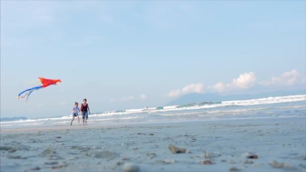 Feliz abuela con el niño el juego volando cometa, la familia corre sobre la arena de un océano tropical jugando con la cometa más vieja. Concepto Infancia feliz y despreocupada . — Vídeo de stock