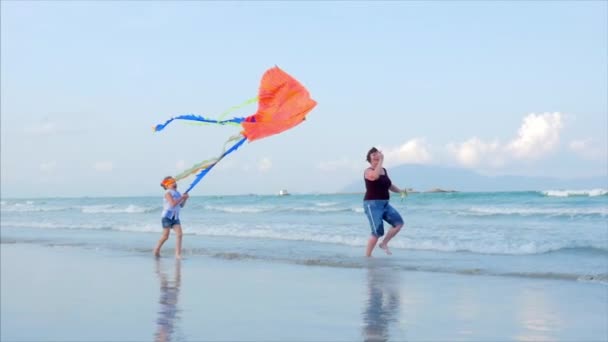 Счастливая бабушка с ребёнком - играющий воздушный змей, семья бежит по песку тропического океана, играя со старым воздушным змеем. Счастливое и беззаботное детство . — стоковое видео