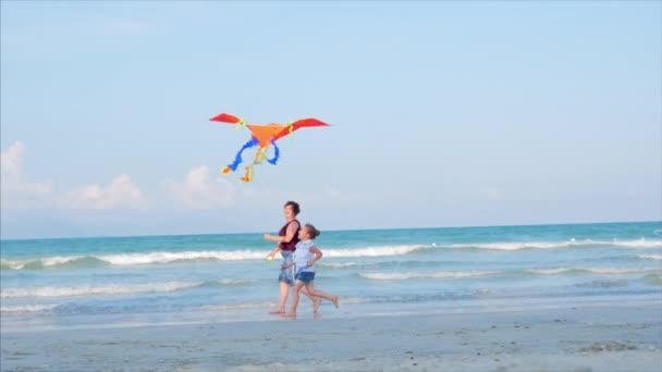 Glückliche Großmutter mit Kind den spielenden Drachen, die Familie läuft auf dem Sand eines tropischen Ozeans und spielt mit dem älteren Drachen. Konzept einer glücklichen und unbeschwerten Kindheit. — Stockvideo