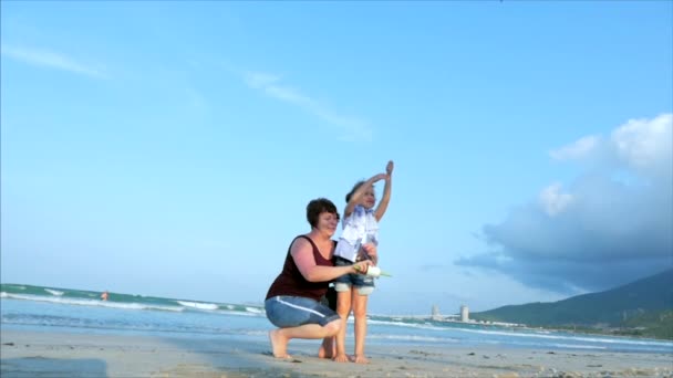 아이와 함께 행복한 할머니는 비행 연을 재생, 가족은 오래된 연과 함께 연주 열대 바다의 모래에 실행됩니다. 개념 행복하고 평온한 어린 시절. — 비디오