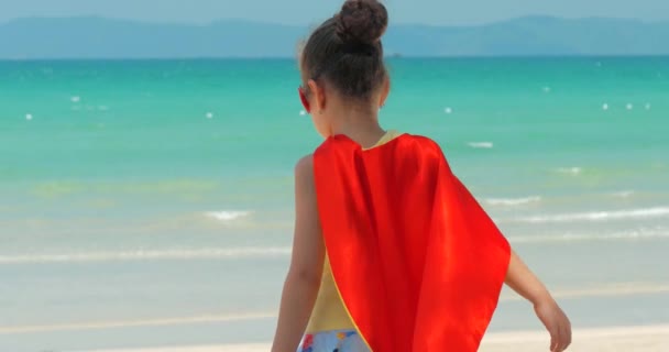 Aranyos kislány a szuperhős jelmez, öltözött a Red Cloak és a maszk a hős. Játszik a háttérben tenger és a Blue Sky és a felhők. A Happy chilhood koncepciója.