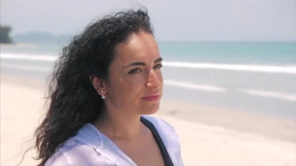 En una playa tropical Primer plano Retrato de europea hermosa linda morena joven mujer o alegre chica mirando en la cámara, soplando viento pelo el viento, cámara lenta . — Vídeos de Stock