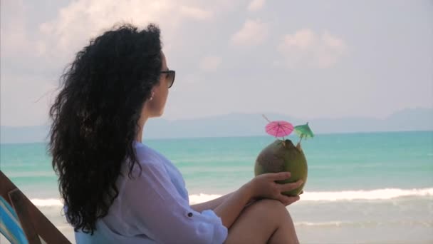 Retrato de una hermosa morena linda europea Mujer joven o una chica alegre, beber un coco en el sol, en el viento en una playa tropical. Concepto Verano, vacaciones, viajes . — Vídeos de Stock