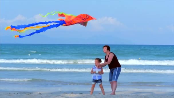 Glückliche Großmutter mit Kind den spielenden Drachen, die Familie läuft auf dem Sand eines tropischen Ozeans und spielt mit dem älteren Drachen. Konzept einer glücklichen und unbeschwerten Kindheit. — Stockvideo