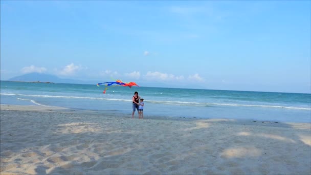 Ευτυχισμένη γιαγιά με το παιδί που παίζει ιπτάμενο χαρταετό, η οικογένεια τρέχει στην άμμο ενός τροπικού ωκεανού παίζοντας με τον παλαιότερο χαρταετό. Ιδέα Happy και ανέμελη παιδική ηλικία. — Αρχείο Βίντεο