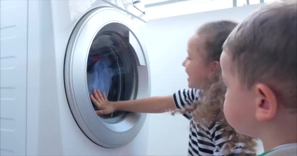 Милые дети заглядывают в стиральную машину. Крутящаяся цилиндрическая машина. Концепция стиральная машина, прачечная . — стоковое видео