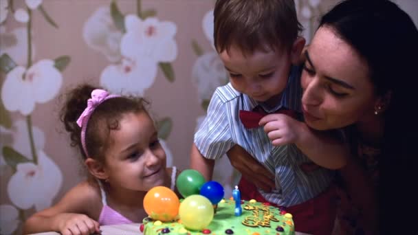 Conceito de uma família feliz. Menino feliz de dois anos comemora seu aniversário com sua família, sua mãe e irmã mais nova o ajudaram a apagar as velas . — Vídeo de Stock