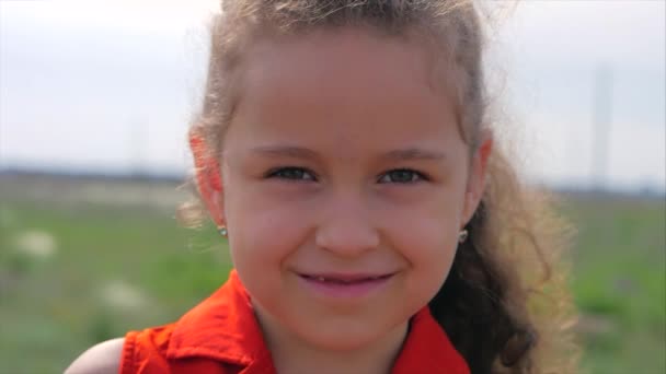 Κοντινό πορτραίτο χαριτωμένο χαρούμενο καυκάσιο μικρό κορίτσι χαμογελάει κοιτάζοντας την κάμερα, απολαμβάνοντας ζεστές καλοκαιρινές διακοπές ηλιόλουστη μέρα. — Αρχείο Βίντεο