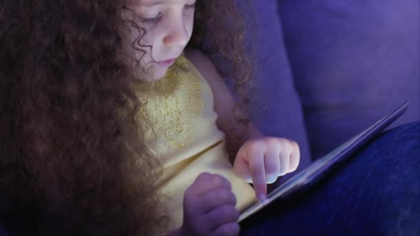 Милый ребенок развлекается с таблеткой. Девочка проводит свободное время, играя в мобильную игру в и сокрушает яркий экран рукой. Концепция: Счастливое детское питание, Технологии, Детские игры — стоковое видео