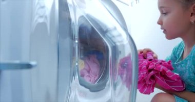 Çamaşır makinesine giysi yükleyin. Küçük Kız Çamaşır Makinesi çamaşır yükler ve yıkama içerir. Konsept Çamaşır Yıkama Makinesi, Sanayi Çamaşırhane Servisi.