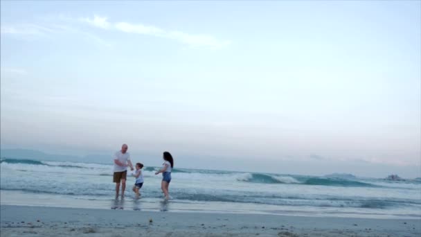 Glückliche Familie mit Kind starten einen Drachen, Mutter Vater und Tochter spielen mit dem älteren Drachen im Hintergrund des Ozeans bei Sonnenuntergang. Konzept einer glücklichen und unbeschwerten Kindheit. — Stockvideo