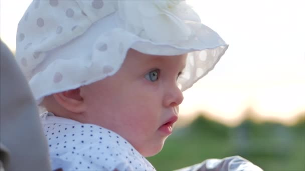 Close-Up al rallentatore girato di cinque mesi Baby Girl seduta all'aperto in un passeggino a guardare la fotocamera. Guarda il bambino nella telecamera da vicino. Concetto di Infanzia, bambino, bambini . — Video Stock