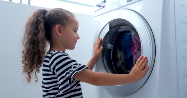 Χαριτωμένο παιδί κοιτάζει μέσα στο πλυντήριο ρούχων. Κύλινδρος περιστρεφόμενοι μηχανές. Ιδέα πλυντηρίου ρούχων, βιομηχανική υπηρεσία πλυντηρίου. — Αρχείο Βίντεο