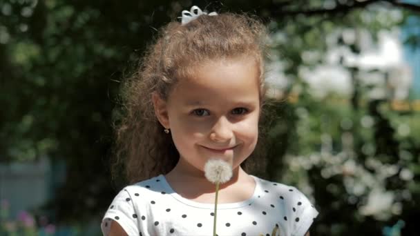 Slow Motion zbliżenie strzał Cute Little Girl beztroski dmuchanie mniszka na zewnątrz na zachód słońca. Koncepcja szczęśliwego Beztrowolnego dzieciństwa. — Wideo stockowe