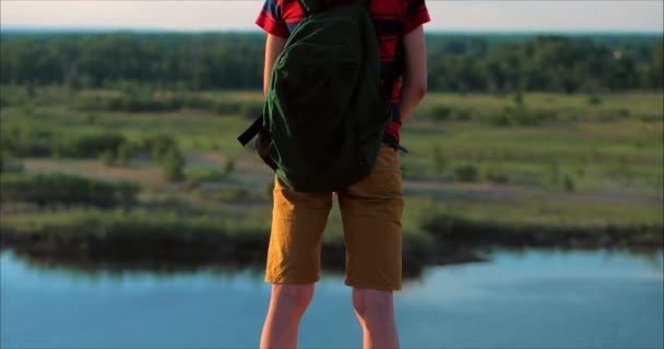 Bei Sonnenuntergang Kind in rotem Hemd mit Rucksack auf dem Rücken, hoch oben auf einem hohen Hügel und Blick auf die Wolken am Himmel, Natur, oben auf einem Berg stehend, erhobene Hände, Erfolgserlebnis — Stockvideo
