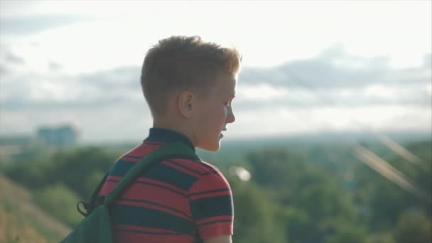 De cerca Retrato Caucásico Niño Adolescente en una camisa roja con una mochila en la espalda, al atardecer, sentado en una colina disfrutando de unas cálidas vacaciones de verano . — Vídeo de stock