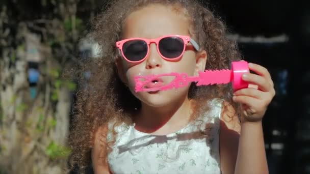 Happy Little Girl jugando al aire libre, soplando burbujas de jabón, divirtiéndose en el patio trasero. Naturaleza. Hermosa niña en el parque . — Vídeo de stock