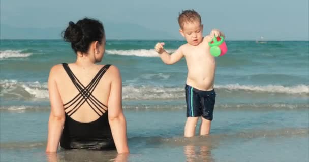 Ευτυχισμένος και ανέμελη μητέρα και γιος παίζουν δίπλα στη θάλασσα, ηλιοθεραπεία, κολύμπι. Παιδιά και ενήλικες παίζουν δίπλα στη θάλασσα σε μια τροπική παραλία. Concept ευτυχισμένη οικογένεια. — Αρχείο Βίντεο