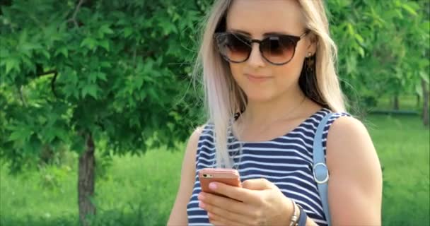 Mujer joven feliz con gafas escribiendo mensajes de texto en el dispositivo del teléfono . — Vídeos de Stock