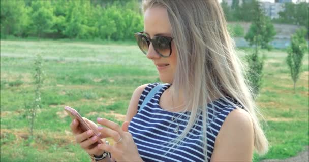 携帯電話のデバイスにテキストメッセージを入力するメガネを持つ幸せな若い女性. — ストック動画