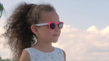Pembe gözlük güzel bir küçük kız yakın çekim portre, sevimli gülümseyen, mavi gökyüzü bakıyor. Konsept: çocuk, çocukluk, yaz, Bebek, Toddler.