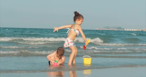 Enfants heureux et insouciants jouant au bord de la mer avec du sable. Enfants jouant, frère et sœur jouant au bord de la mer. Bonne enfance . — Video