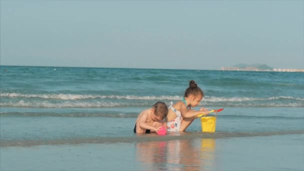 Ευτυχισμένα και ανέμελα παιδιά που παίζουν δίπλα στη θάλασσα με άμμο. Τα παιδιά παίζουν, τα αδέρφια παίζουν δίπλα στη θάλασσα. Ευτυχισμένη παιδική ηλικία. — Αρχείο Βίντεο