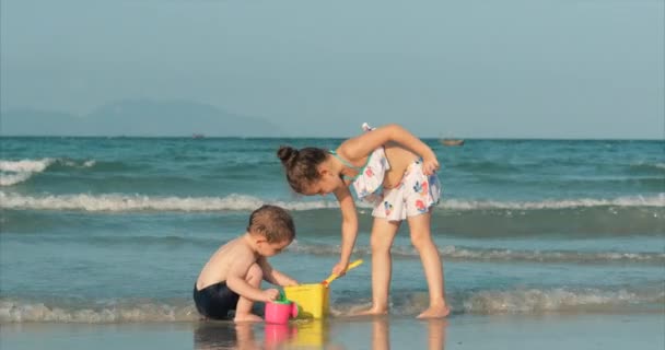 Ευτυχισμένα και ανέμελα παιδιά που παίζουν δίπλα στη θάλασσα με άμμο. Τα παιδιά παίζουν, τα αδέρφια παίζουν δίπλα στη θάλασσα. Ευτυχισμένη παιδική ηλικία. — Αρχείο Βίντεο