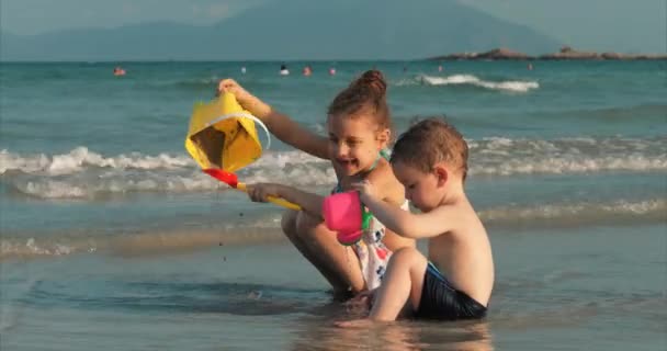 Счастливые и беззаботные дети играют на берегу моря с песком. Дети играют, брат и сестра играют у моря. Счастливое детство . — стоковое видео