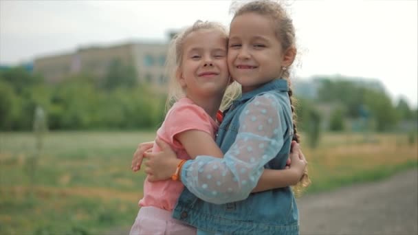 Dos hermanas sonrientes, rizadas y lindas se abrazan con fuerza. Feliz infancia, emociones positivas, sentimientos verdaderos . — Vídeos de Stock