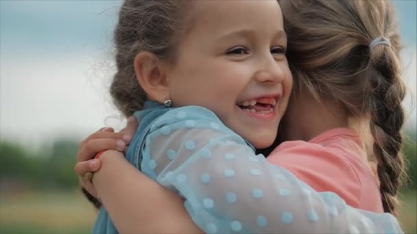 Dos hermanas sonrientes, rizadas y lindas se abrazan con fuerza. Feliz infancia, emociones positivas, sentimientos verdaderos . — Vídeos de Stock
