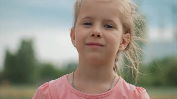 クローズアップポートレートかわいい幸せな白人の小さな女の子は、カメラを見て微笑み、暖かい夏休み晴れた日を楽しんで. — ストック動画