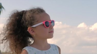 Pembe gözlük güzel bir küçük kız yakın çekim portre, sevimli gülümseyen, mavi gökyüzü bakıyor. Konsept: çocuk, çocukluk, yaz, Bebek, Toddler.