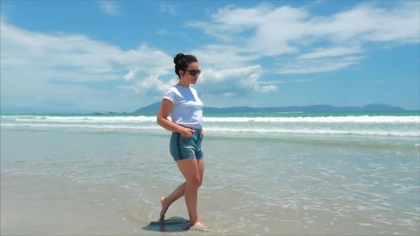 Σε μια τροπική παραλία όμορφη σκηνή μιας γυναίκας που περπατάει στην παραλία του ωκεανού στο ηλιοβασίλεμα. Κοντινό πλαίσιο των γυναικών ποδιών Ευρωπαϊκή όμορφη μελαχρινή, περπάτημα κατά μήκος της παραλίας, αργή κίνηση. — Αρχείο Βίντεο