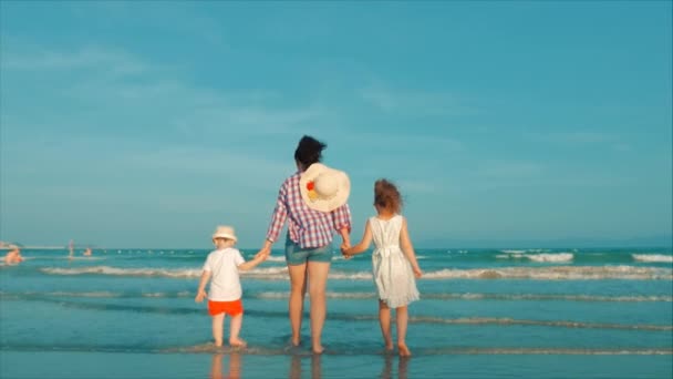シルエット幸せな母と娘と息子が遊んで、夕暮れ時にビーチで楽しんでいます。スローモーション。ハッピーファミリー子供時代の自由と旅行の概念. — ストック動画