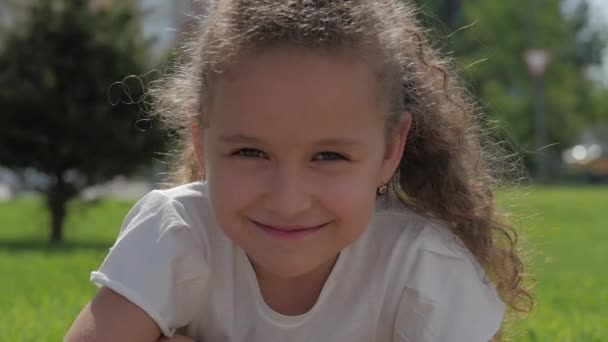 Close-up portret schattig gelukkig Kaukasische meisje glimlachend op zoek naar de camera, genieten van warme zomer vakantie zonnige dag. — Stockvideo