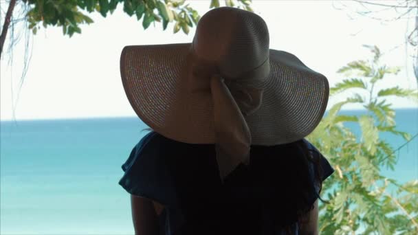 Maravilloso retrato de una mujer caucásica con un sombrero grande, mujer con sombrero de pie en su balcón con vista al mar. Enfoque suave — Vídeos de Stock