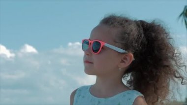 Pembe gözlük güzel bir küçük kız yakın çekim portre, sevimli gülümseyen, mavi gökyüzü bakıyor. Konsept: çocuk, çocukluk, yaz, Bebek, Toddler.
