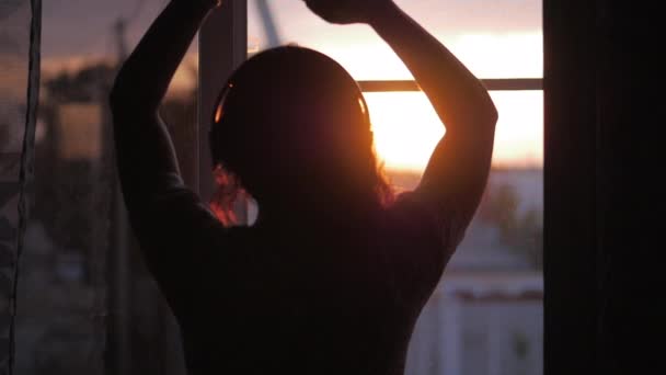 Portrait Attractive Young Woman Listening to Music with Headphones, a Girl or a Woman Looking Out the Window Listening to Music at Sunset. — Stock Video