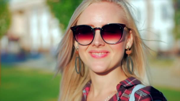 Porträt einer süßen Blondine mit Sonnenbrille, junge glückliche Frau oder fröhliches Mädchen, das in die Kamera schaut, Wind weht Haare im Wind, Zeitlupe. — Stockvideo