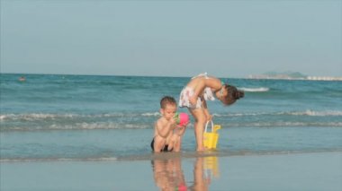 Mutlu ve kaygısız çocuklar kumla deniz kenarında oynuyorlar. Çocuklar oynuyor, erkek ve kız kardeşler deniz kenarında oynuyor. Mutlu Çocukluk.
