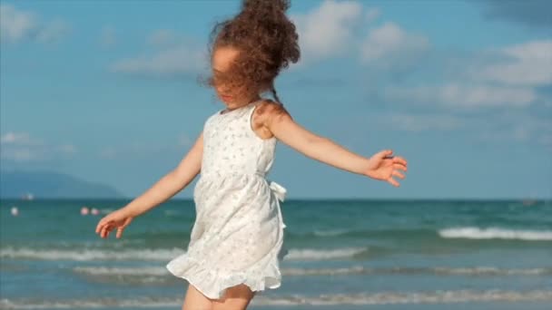 Šťastná dívka tančí na tropickém pobřeží podél pláží na pozadí tropického oceánu. Koncepce: děti, šťastné dětství, léto, dítě, dovolená. — Stock video