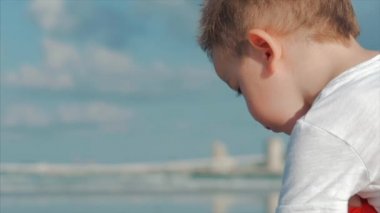 Sevimli Küçük Çocuk Deniz kenarında oynar, Çocuk Yakalar, Mavi Okyanusa Karşı Tropikal Bir Plajda Canlı Deniz Kabukları, Yengeçler, Düşünüyor. Konsept: Çocuk, Mutlu Çocukluk, Yaz, Çocuk, Tatil. Yumuşak odaklama