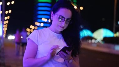 Pretty Woman beyaz bir t-shirt ve gözlük sokakta duruyor, kredi kartı ve akıllı telefon, online alışveriş teknolojisi ile online ödemeler yapar. Kredi kartı ve cep telefonu ile satın alma için ödeme.