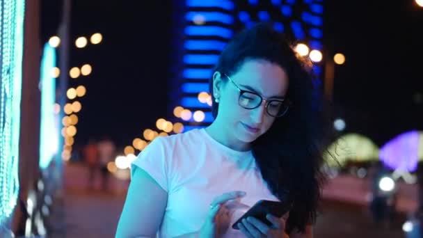 Pretty Woman se encuentra en la calle en una camiseta blanca y gafas, hace pagos en línea con tarjeta de crédito y teléfono inteligente, tecnología de compras en línea. Pago por compra con tarjeta de crédito y teléfono móvil . — Vídeo de stock