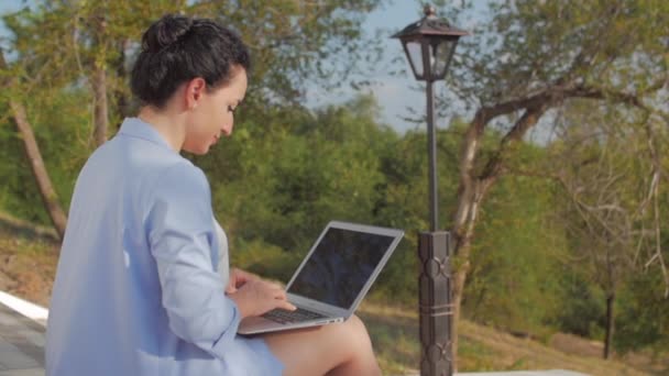 Obchodní žena pracující na přenosném počítači, přitažlivá bruneta v modrém obleku s notebookem, atraktivní dáma pracující na svém počítači venku. — Stock video